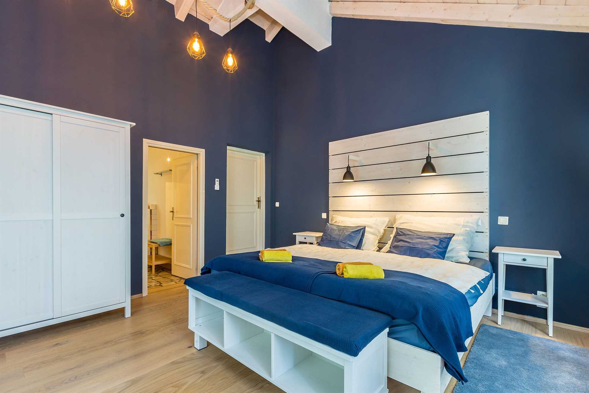 Modra spavaća soba s krevetom, podnožjem i ormarom.