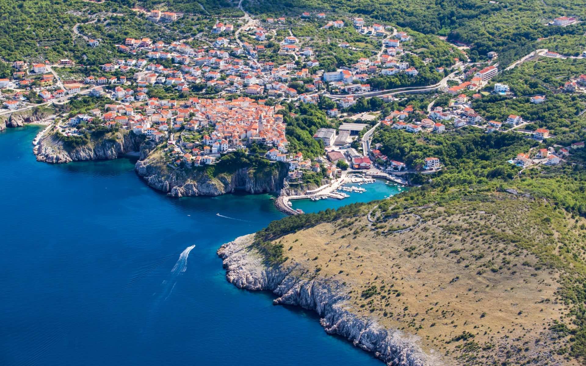 Aerial view of the town of Vrbnik perched on a hill with the sea and harbor below.
